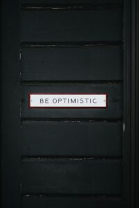 black wooden door with be optimistic text overlay